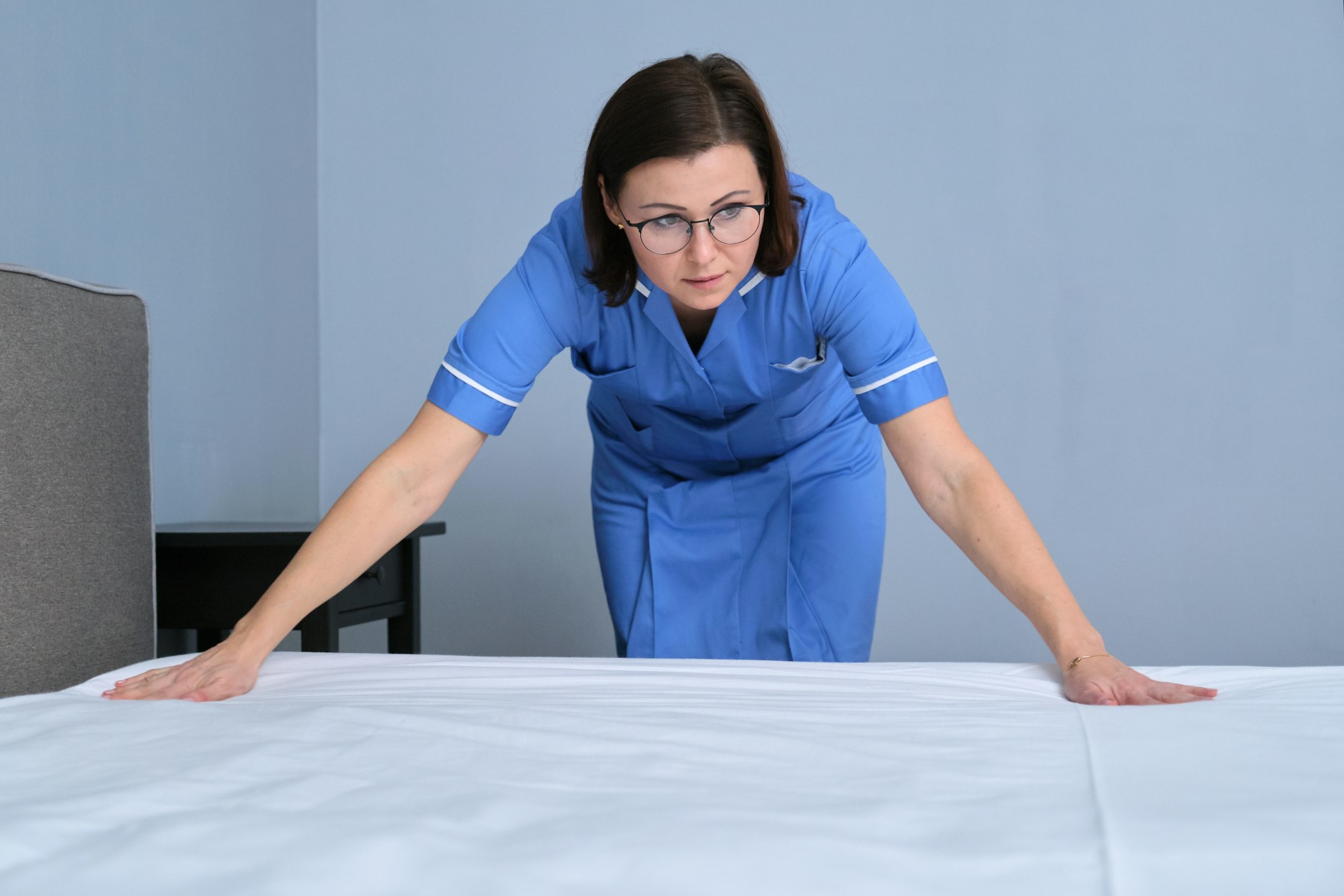 Cleaning service in hotel room, woman maid preparing guest room making bed